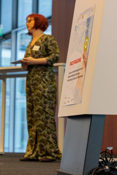 Frau Denise Gramß vom Forschungsinstitut Betriebliche Bildung (f-bb) gGmbH steht einen auf einem Podium. Sie trägt einen grün-Schwarz-gemusterten Jumpsuit.
