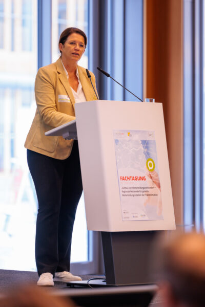 Frau Christina Ramb (Mitglied der Hauptgeschäftsführung der Bundesvereinigung der Deutschen Arbeitgeberverbände (BDA) steht auf einem Podium hinter einem Pult mit Mikrofon. Sie trägt einen beigefarbenen Blazer und eine schwarze Hose.
